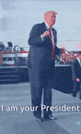 a man in a suit and tie is standing on a stage with the words " i am your president " written below him