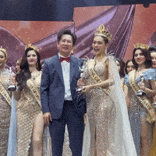 a man in a suit stands next to a woman wearing a sash that says ' miss asia '