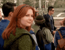 a woman with red hair is standing in a crowd of people looking at the camera .