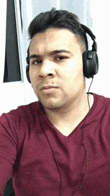 a man wearing headphones and a maroon shirt is taking a selfie
