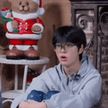 a young man wearing glasses is sitting on the floor in front of a stuffed teddy bear .