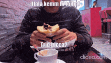 a man is sitting at a table eating a donut with a caption that says " illala kemm hi tajba "