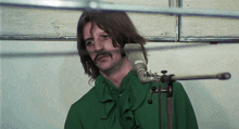 a man with a green shirt and a mustache is standing in front of a microphone