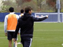 a man pointing at something on a soccer field with a red bull banner behind him