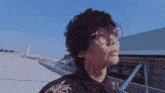 a man with curly hair and glasses stands on a rooftop