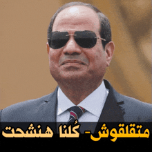 a man in a suit and tie wearing sunglasses with arabic writing underneath him