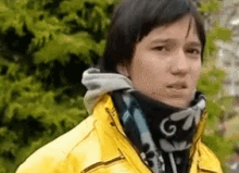 a man wearing a yellow jacket and a scarf around his neck looks at the camera .