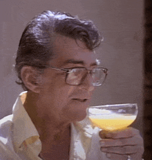a man with glasses is drinking a glass of orange juice