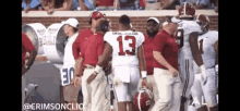 a football player with the number 13 on his jersey is talking to a coach on the sidelines .