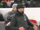 a man wearing a black nike jacket with a green axa logo on it