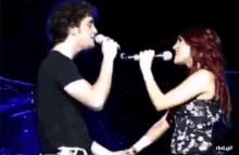 a man and a woman are singing into microphones on stage .
