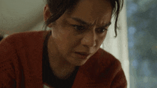 a woman in a red sweater looks at the camera with a serious look on her face