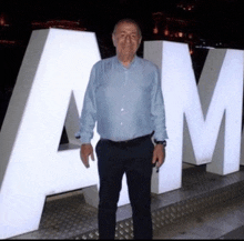 a man in a blue shirt is standing in front of a large white letter m