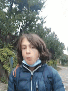 a young boy wearing a mask and a blue jacket looks at the camera