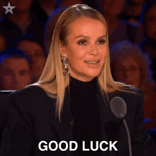 a woman speaking into a microphone with the words " good luck " behind her
