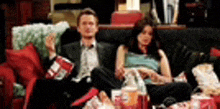 a man and a woman are sitting on a couch eating popcorn and watching a movie .