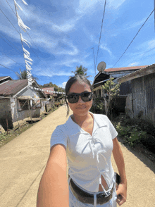 a woman wearing sunglasses is taking a selfie in a small village
