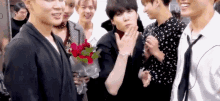 a group of young men are standing around a man holding a bouquet of roses .