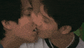 two young men are kissing each other on the cheek . one of the men is wearing a pearl necklace .