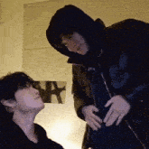 a man in a hooded jacket is touching the belly of another man in a black jacket