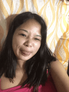 a woman in a pink tank top is sticking her tongue out in front of a yellow and white curtain