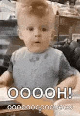 a baby is sitting at a table and making a funny face while wearing a bib .