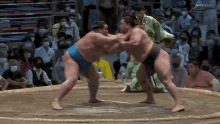 two sumo wrestlers are fighting in a ring with a crowd watching .