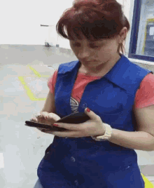 a woman wearing a blue vest is holding a cell phone
