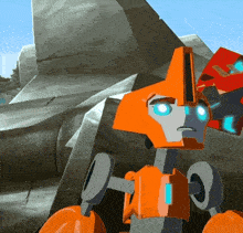 an orange robot with blue eyes is standing in front of a large rock
