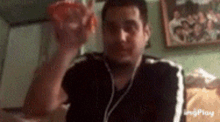 a man wearing headphones is holding a red object in his hand in front of a picture of a family .
