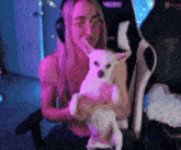 a woman is holding a small white dog in her arms while sitting in a gaming chair