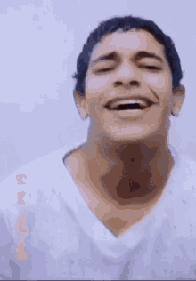 a man in a white shirt is laughing with his mouth open and his eyes closed .
