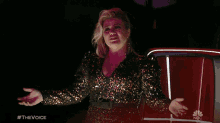 a woman in a sequined dress is standing in front of a red car with #thevoice written on the bottom