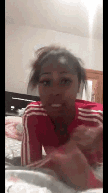 a woman in a red and white adidas shirt is laying on a bed