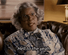 a woman with glasses is sitting on a couch and says hell to the yeah .