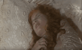 a woman with red hair is laying on a bed with her eyes closed and a white blanket .