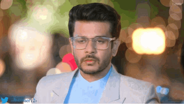 a man wearing glasses and a suit is standing in front of a twitter logo