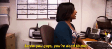 a woman is sitting at a desk saying screw you guys you 're dead to me .