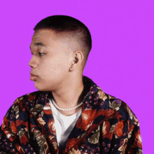 a man wearing a floral shirt and a pearl necklace looks to the side