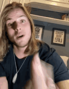 a man with long blonde hair is standing in front of a wall that has a sign that says " i feel "