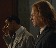 two men in suits are standing next to each other and one is covering his nose