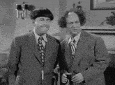 a black and white photo of two men in suits and ties standing next to each other in a living room .
