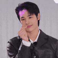a young man in a black leather jacket is making a heart shape with his finger