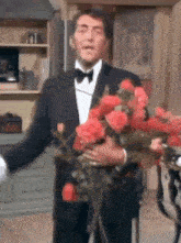 a man in a tuxedo is holding a bouquet of red roses in his hands .