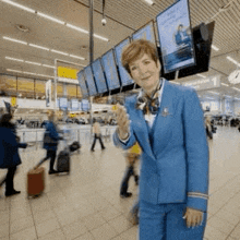 a woman in a blue suit is standing in a crowded airport terminal .