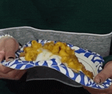 a person is holding a blue and white paper plate with macaroni and cheese on it