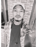 a man wearing a plaid shirt and a hat takes a selfie in front of a brick wall