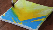 a person is painting a yellow and blue painting on a canvas .