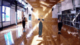 two women are dancing in a large room with a viggle.ai logo on the bottom