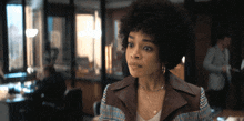 a woman with curly hair is wearing a plaid jacket and a gold necklace